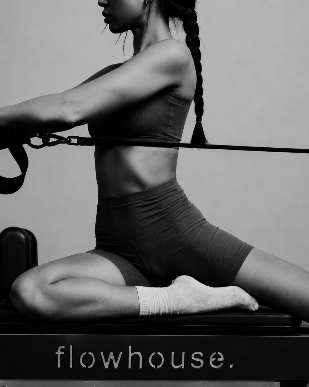 Sam, founder of flowhouse, holding hand weights overhead in a strong, grounded stance — a warm-toned editorial black-and-white campaign image.