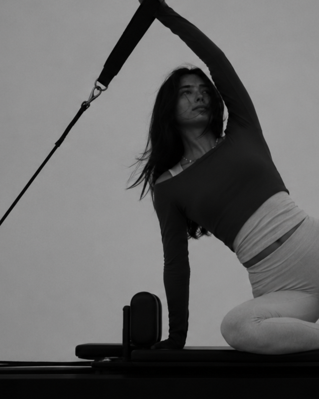 Sam, founder of flowhouse, holding hand weights overhead in a strong, grounded stance — a warm-toned editorial black-and-white campaign image.