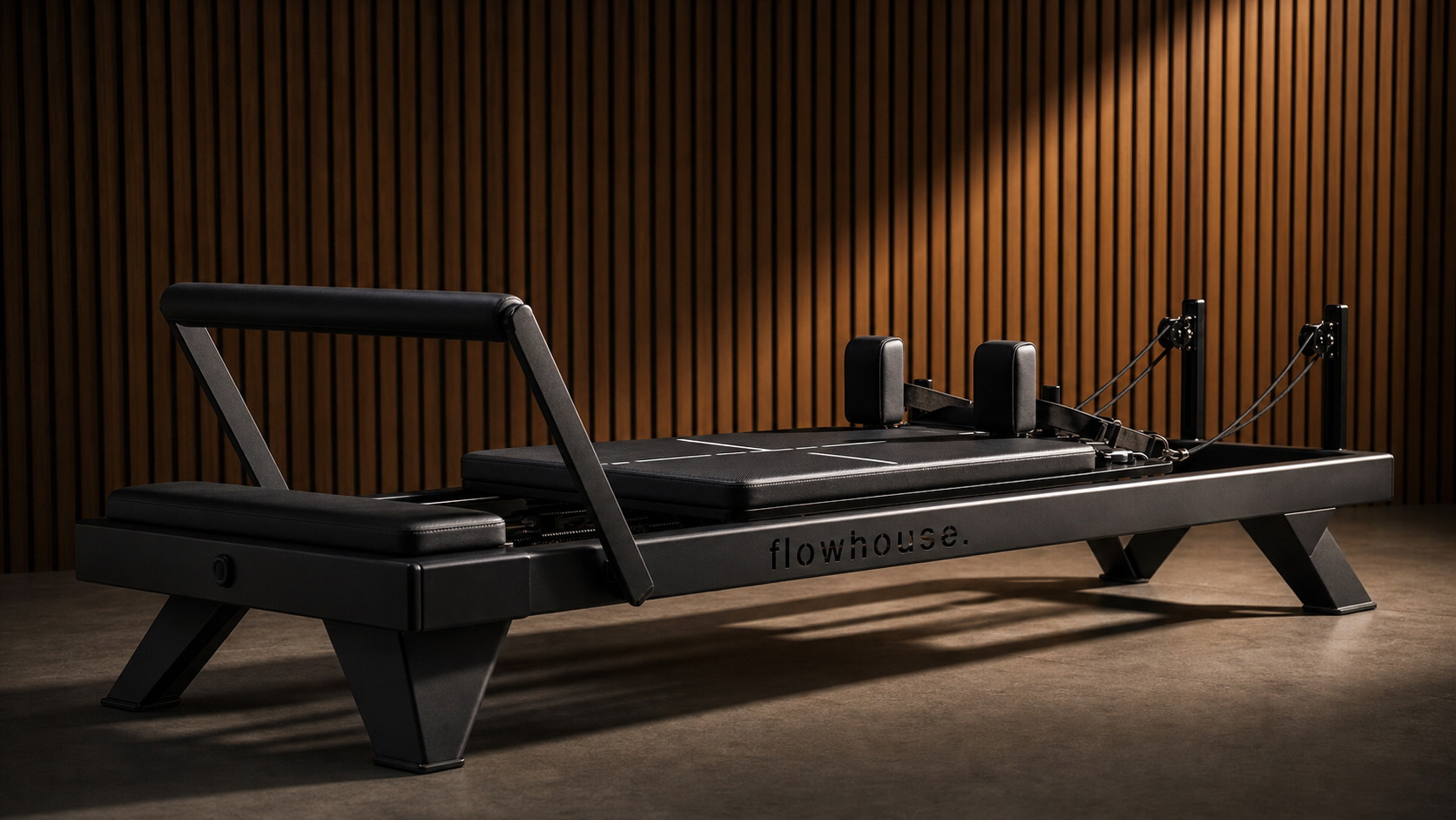 The custom Flowformer reformer — matte-black tubular steel with the flowhouse. wordmark cut out as negative-space on the side rail.