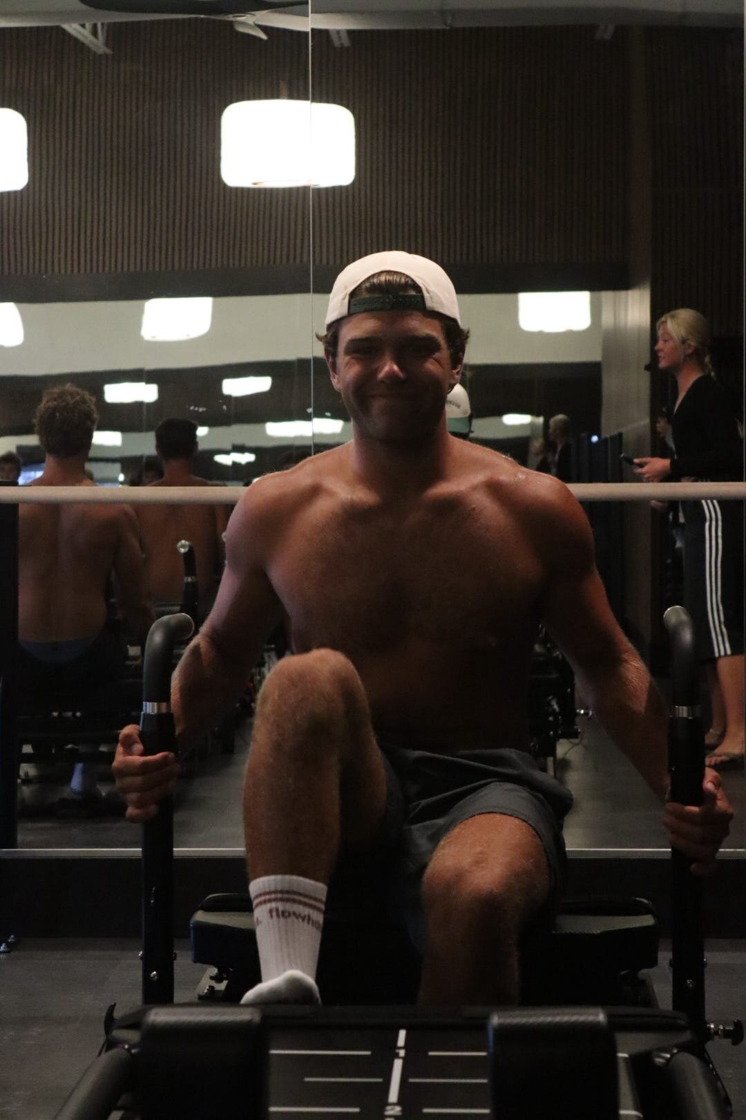 A flowhouse member seated on the FlowFormer reformer in flowhouse grip socks, reflected in the mirrored studio wall.