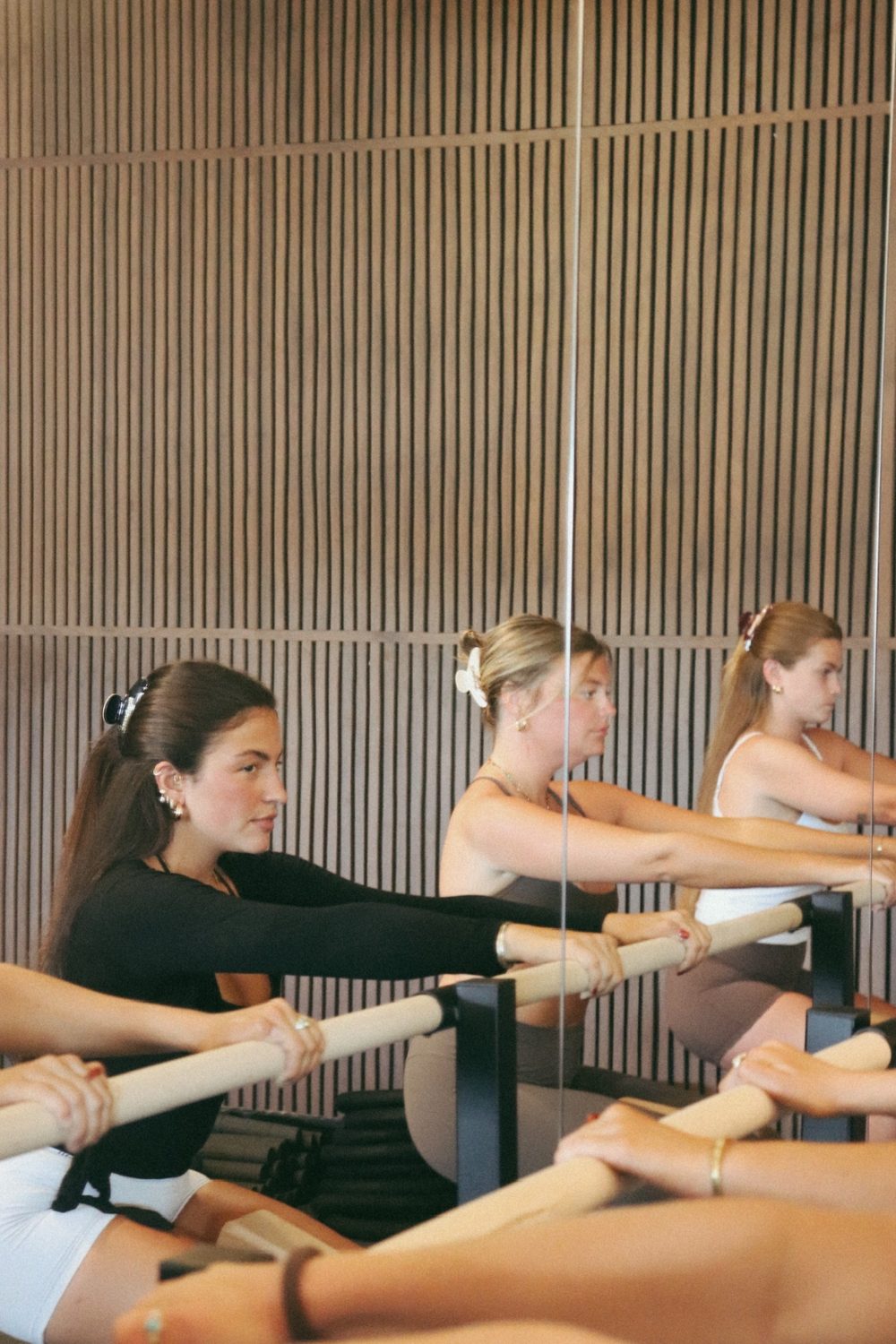 Members reaching through a barre stretch against the warm walnut feature wall.