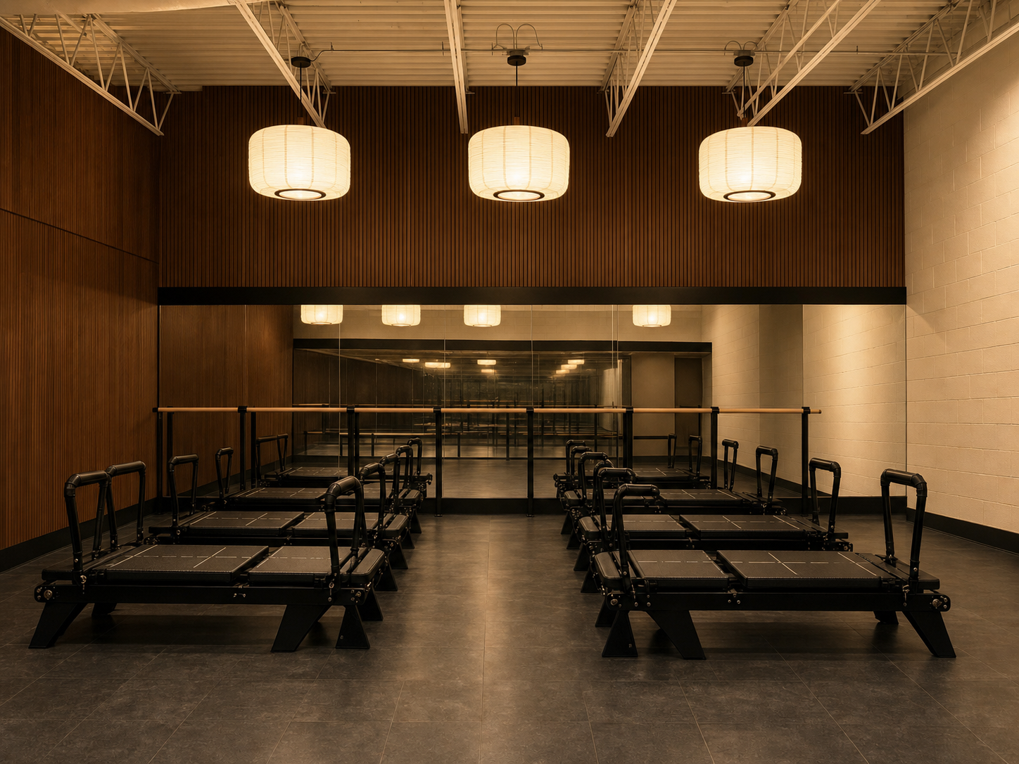 The flowhouse studio — warm walnut wood-slat walls, three glowing pendant lanterns, and ten custom Flowformer reformers arranged in two rows facing the mirrored barre wall.